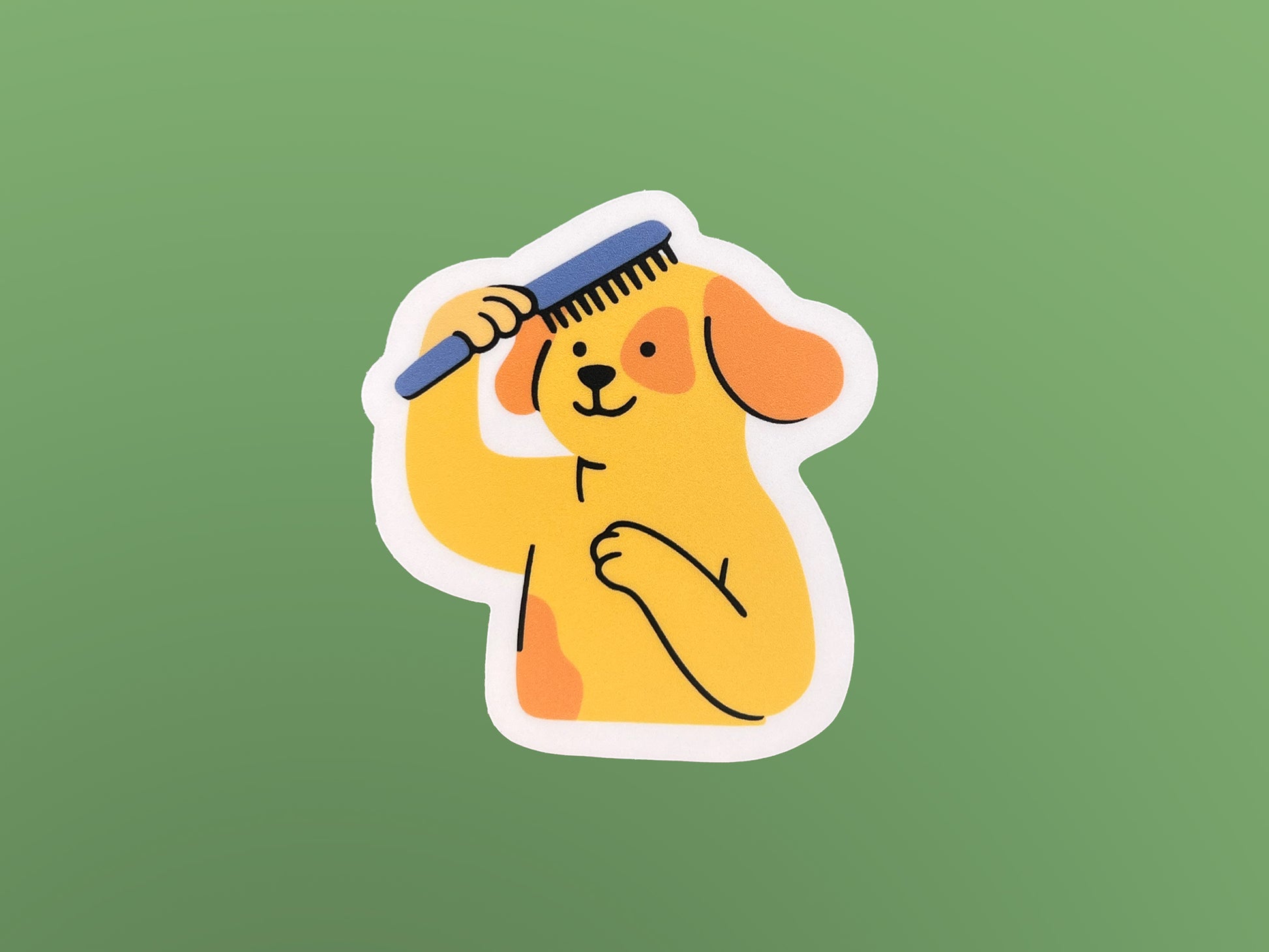 Illustrated yellow dog brushing its own hair with a blue comb, shown as a matte die cut vinyl sticker with floppy orange ears and one paw on its chest. The sticker has a soft pink border and is displayed on a green background, highlighting the playful design and compact size.