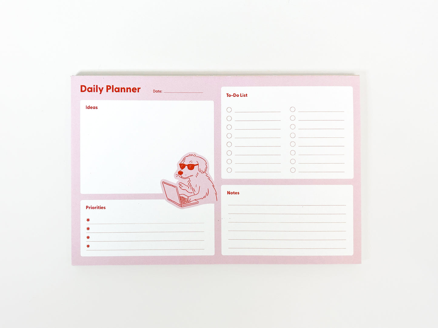 Flat lay of a pink daily planner notepad on a white background, showing the full layout with sections labeled Daily Planner, Ideas, Priorities, To-Do List, and Notes. A small illustration of a dog wearing sunglasses and typing on a laptop appears near the center. The planner has a structured, minimalist design intended for daily planning and note-taking.