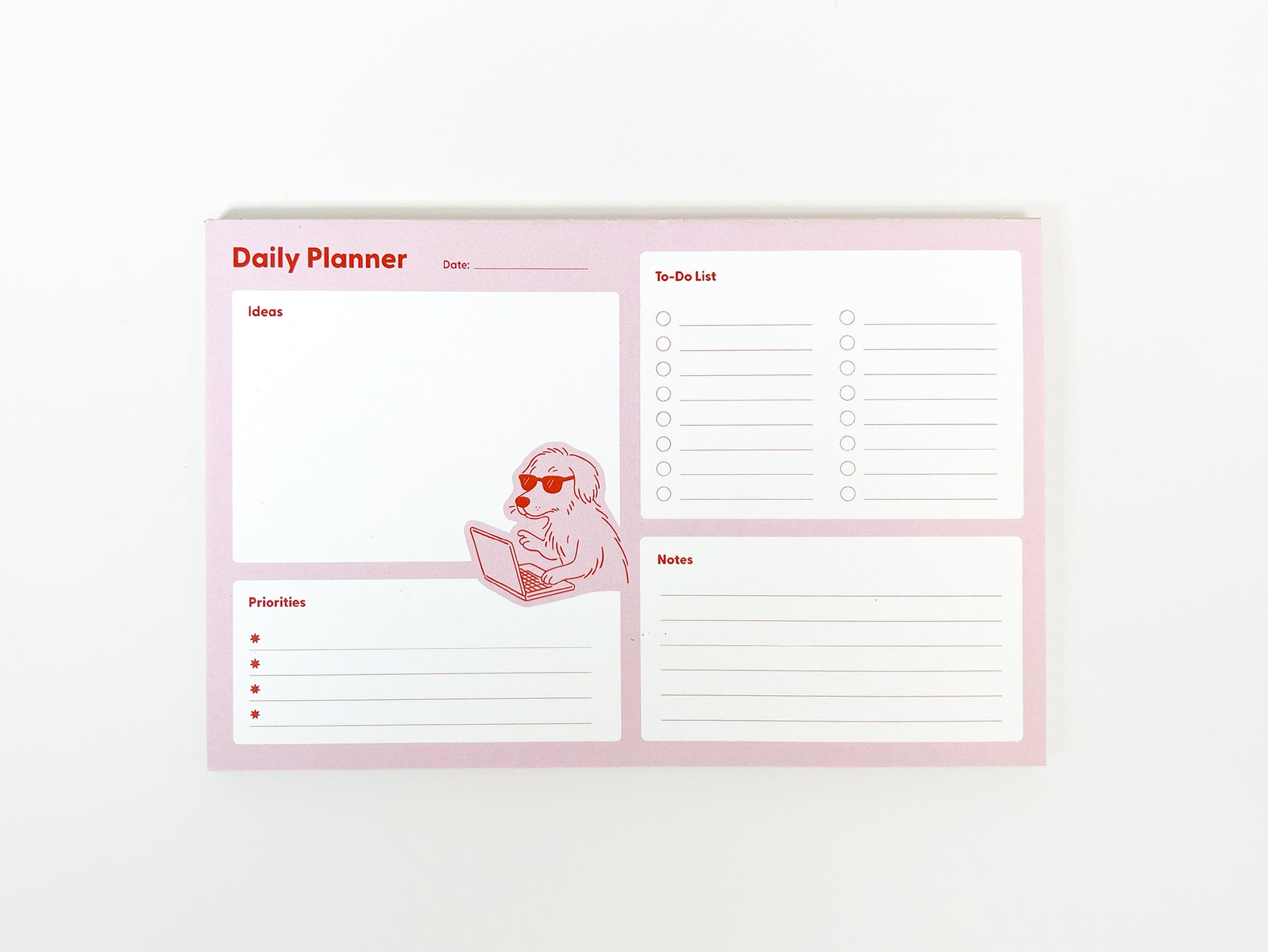 Flat lay of a pink daily planner notepad on a white background, showing the full layout with sections labeled Daily Planner, Ideas, Priorities, To-Do List, and Notes. A small illustration of a dog wearing sunglasses and typing on a laptop appears near the center. The planner has a structured, minimalist design intended for daily planning and note-taking.