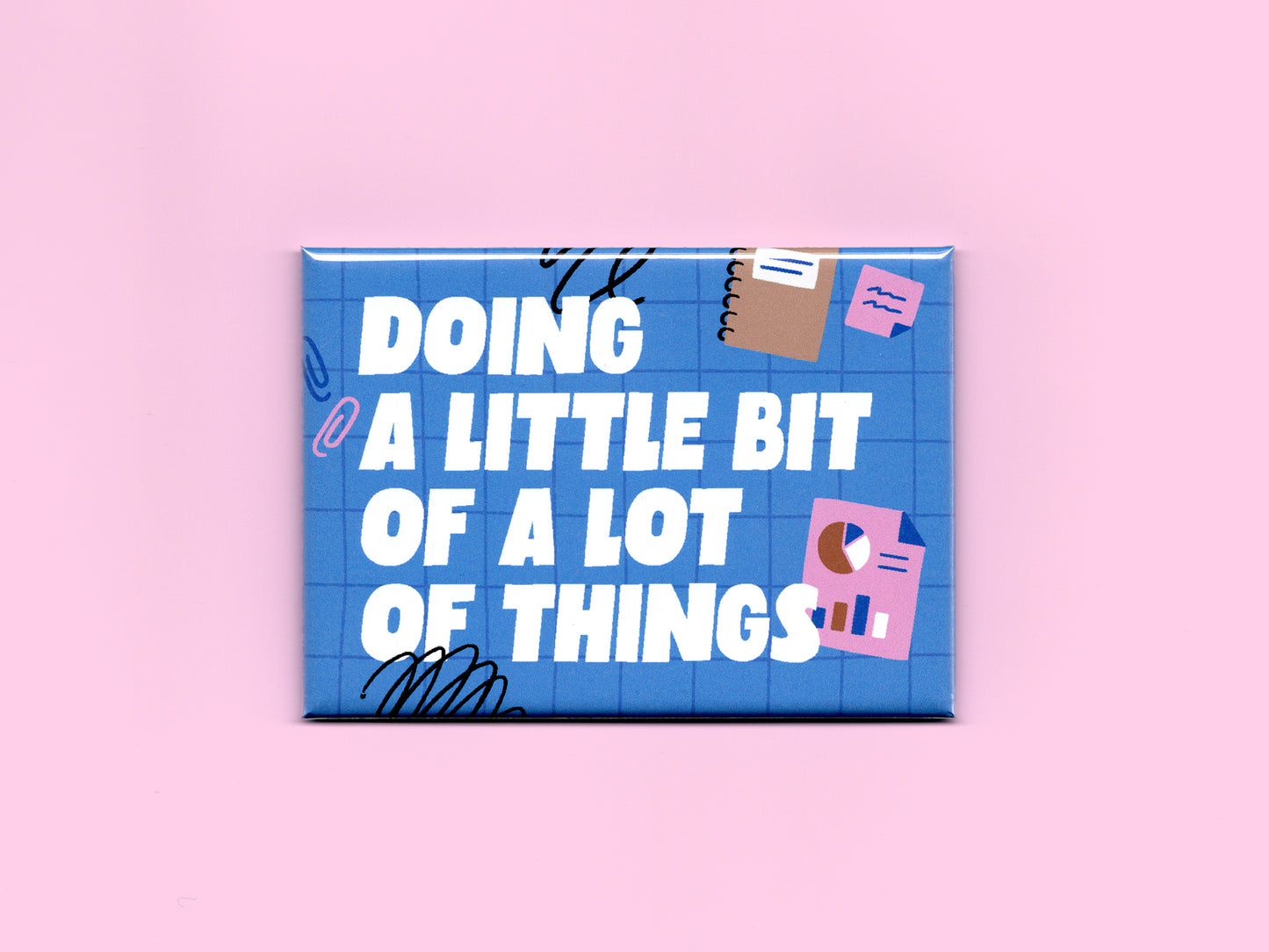 Blue rectangular magnet on a pink background with bold white text reading “Doing a Little Bit of a Lot of Things.” The design features a blue grid pattern with playful office-themed illustrations including sticky notes, charts, paper clips, and black scribble accents.