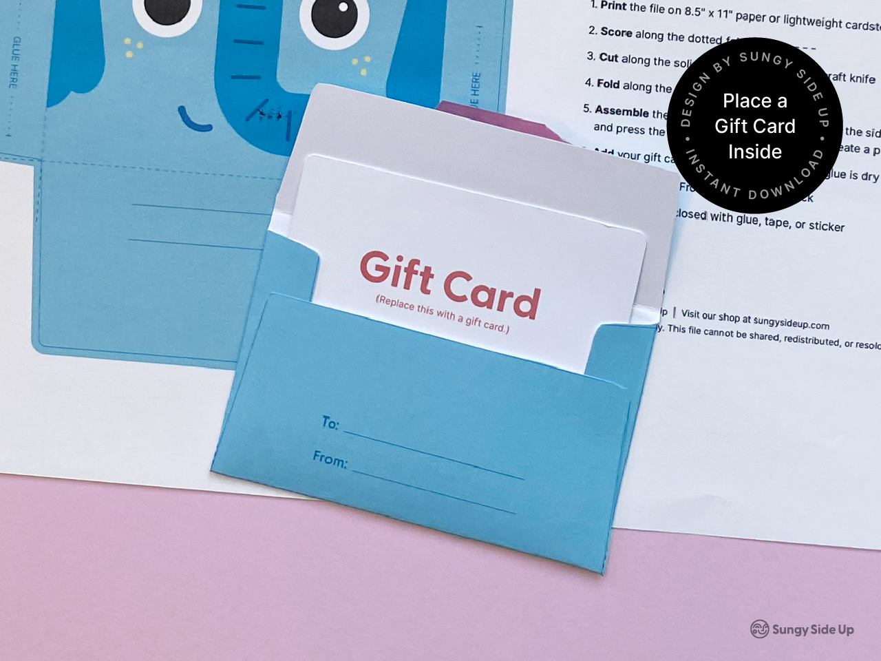 A printed and assembled elephant gift card holder sits open with a mock gift card inserted. The front shows “To” and “From” lines for personalization. Background elements include printed instructions and the flat, uncut elephant template. A circular badge says “Place a Gift Card Inside.” This visual demonstrates how the printable file functions, perfect for birthdays, teacher gifts, and DIY gifting.