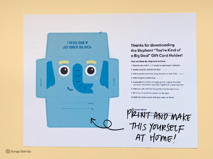 Flat lay of a printable elephant gift card holder on a yellow background. The design features a blue cartoon elephant with big eyes and “You’re Kind of a Big Deal” text. A step-by-step instruction sheet is visible next to the design. Handwritten text on the image says “Print and make this yourself at home!” This image highlights the DIY aspect of the product, ideal for buyers seeking fun and easy printable gifts.