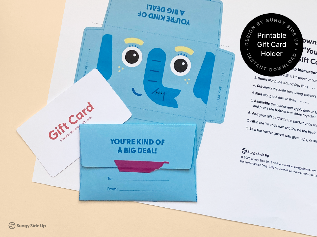 Photo shows a finished elephant-themed gift card holder with “You’re Kind of a Big Deal!” printed on the flap and a blank “To/From” section below. A mock gift card sits beside it, and the printable sheet and instructions are shown in the background. A black circular label highlights that it’s a printable gift card holder. This visual reinforces the personalization feature and fun presentation of the DIY envelope.