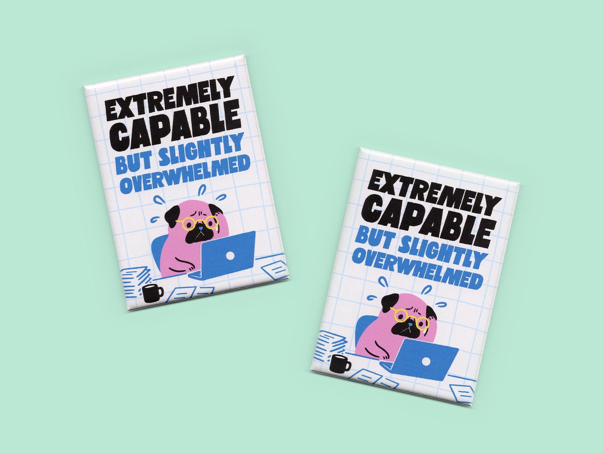 Two rectangular magnets displayed on a mint green background with bold black and blue text reading “Extremely Capable But Slightly Overwhelmed.” Each magnet features an illustration of a stressed pink pug wearing glasses while working on a laptop surrounded by papers and a coffee mug on a white grid background.