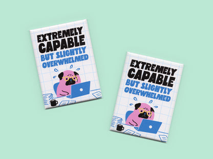 Two rectangular magnets displayed on a mint green background with bold black and blue text reading “Extremely Capable But Slightly Overwhelmed.” Each magnet features an illustration of a stressed pink pug wearing glasses while working on a laptop surrounded by papers and a coffee mug on a white grid background.