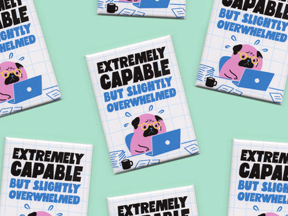 Multiple rectangular magnets displayed on a mint green background with bold black and blue text reading “Extremely Capable But Slightly Overwhelmed.” Each magnet features a stressed pink pug wearing glasses while working on a blue laptop surrounded by papers and a coffee mug on a white grid background.