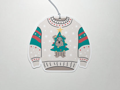 Christmas-themed sweater gift tag. The sweater is designed in light beige with festive decorations. On the front, there is a playful illustration of a small gray schnauzer dog dressed as a Christmas tree, complete with a yellow star on top. The sweater's sleeves feature red and green stripes with white snowflake patterns, matching the overall holiday aesthetic. This cute and festive design would be perfect for holiday gift-giving.