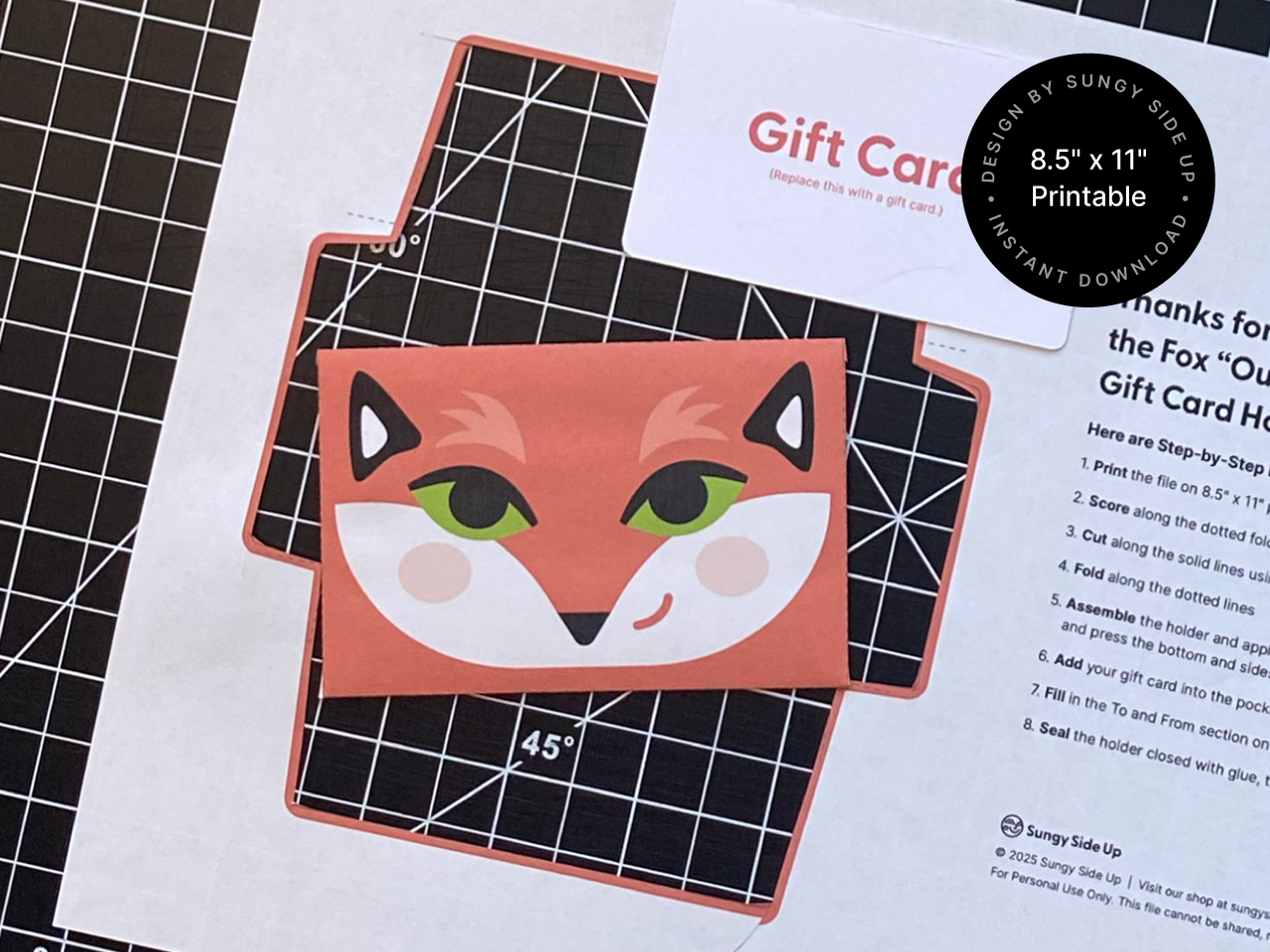 A flat lay of a DIY printable fox gift card holder template placed on a cutting mat, with the assembled envelope featuring a bold fox face design in the center. Ideal for 8.5 x 11 inch paper and perfect for digital downloads, craft projects, or last-minute gifts. Includes step-by-step instructions for printing, cutting, folding, and assembling at home. Great for handmade gifting.