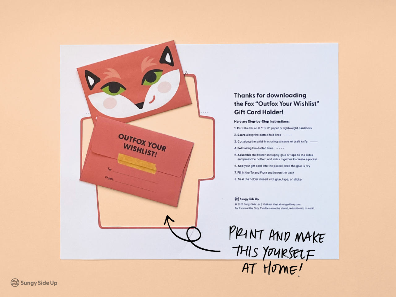 Two views of the completed fox printable gift card holder—front and back—shown on top of the printed template and instruction sheet. The front shows a smiling fox face while the back reads “Outfox Your Wishlist” with space to write To and From. A great DIY craft for kids or gift givers looking for a creative presentation. Easy-to-use, digital download for home printing.