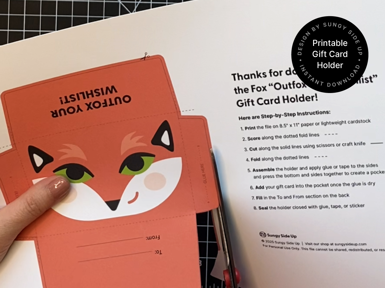 Close-up of a person cutting out the fox gift card holder template with scissors. The template is printed on 8.5 x 11 inch paper and includes a bright fox face and labeled fold lines for simple DIY assembly. Step-by-step directions are visible next to the cutout, showing how easy it is to create a custom envelope at home. Ideal for printable crafts and digital card holder projects.
