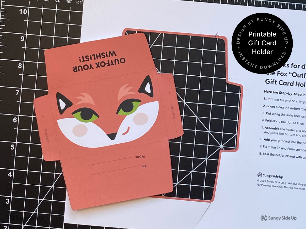 Flat lay of a printable fox gift card holder template on a cutting mat next to printed instructions. The colorful envelope design is partially folded and ready to assemble. Designed for easy DIY use with 8.5 x 11 inch paper or cardstock. A great digital download craft project for creative gift-giving and handmade occasions.