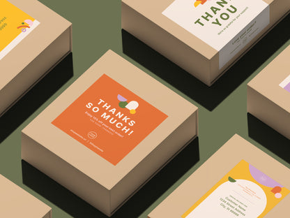 A set of kraft paper product boxes arranged on a muted green background, each featuring colorful printed thank-you and shipping labels on top and sides. The central box shows an orange label reading “THANKS SO MUCH!” in off-white text.
