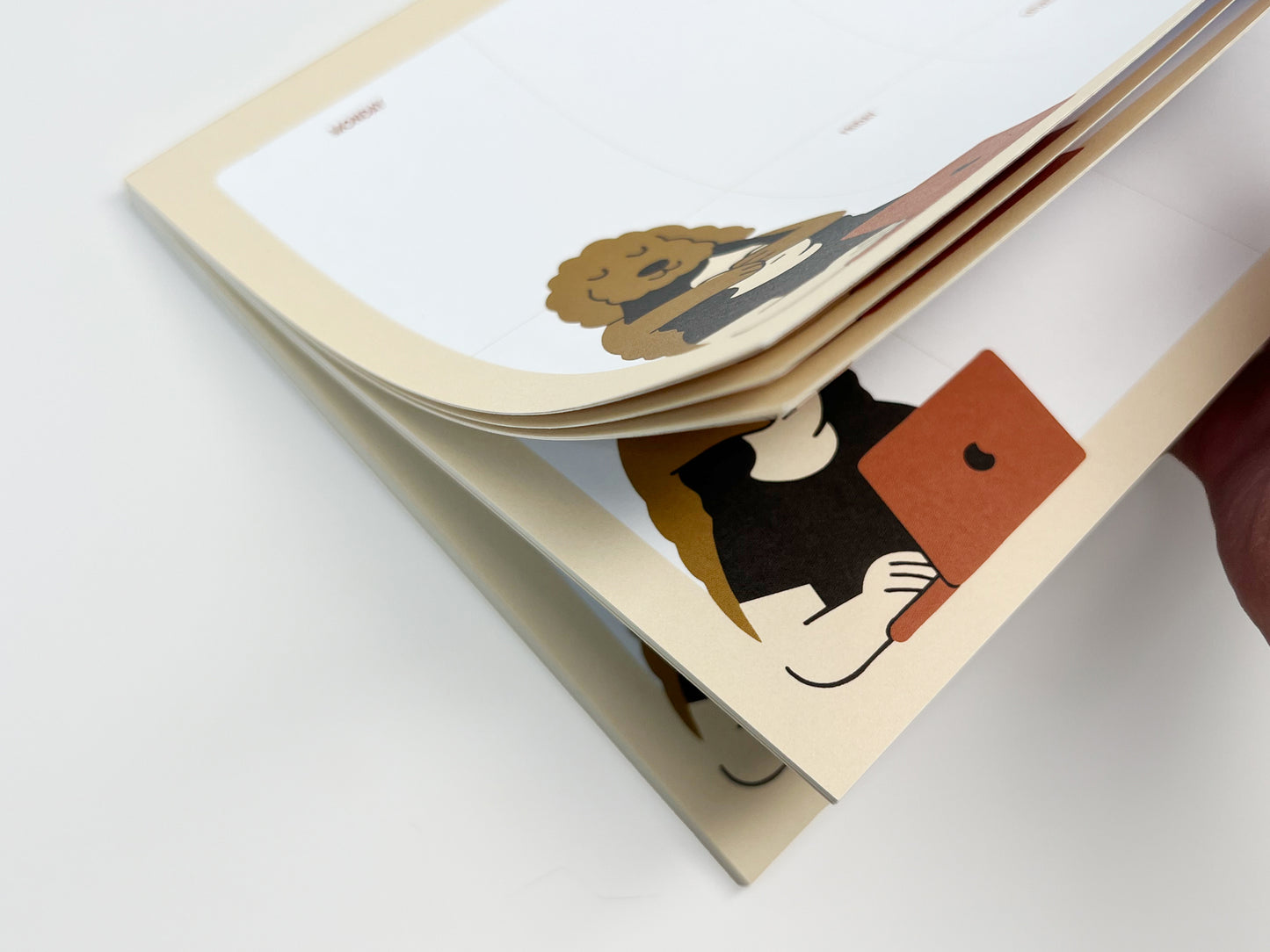 Angled close-up of a weekly planner notepad with several pages slightly lifted, showing thick paper and a clean Monday–Sunday layout. A playful dog illustration appears in the corner of each page as the notepad bends naturally, resting against a white background.
