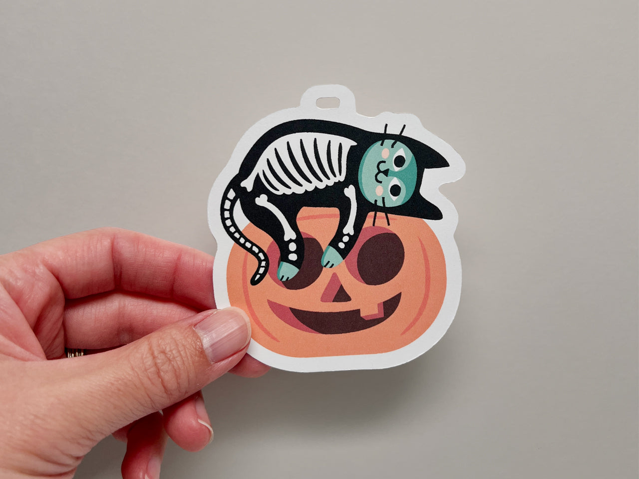 Illustration of a green cat dressed in a skeleton costume resting on top of jack-o-lantern.