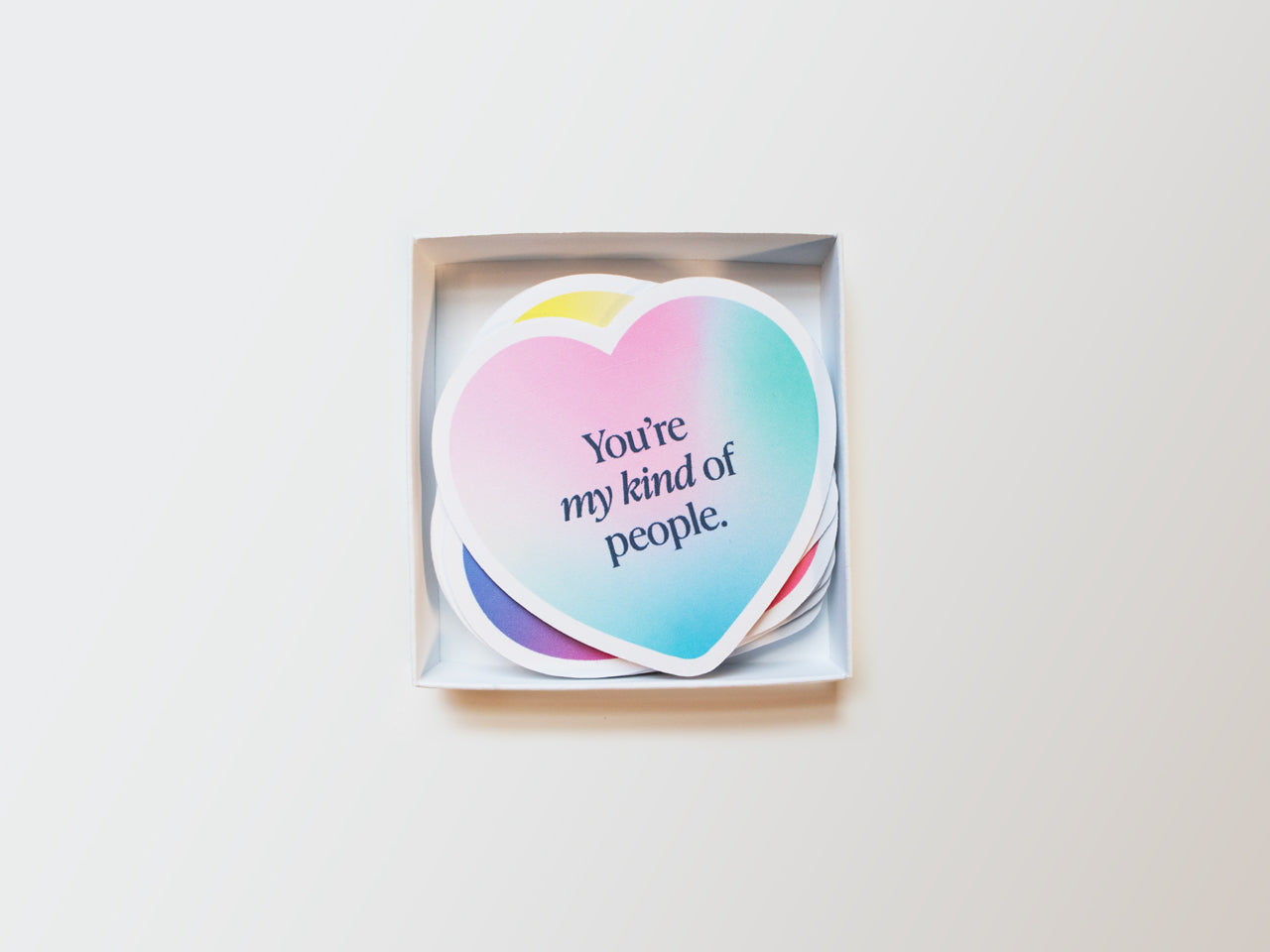 A box of gradient, handmade heart-shaped note cards with an encouraging message on top that reads, You’re my kind of people. The box is open, showing other gradient colored mini notes neatly stacked inside.