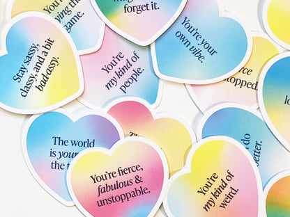 A scattered display of gradient heart-shaped note cards with uplifting messages. The colorful pastel stationery features positive affirmations and motivational quotes, making them perfect encouragement cards for gifting or decorating.