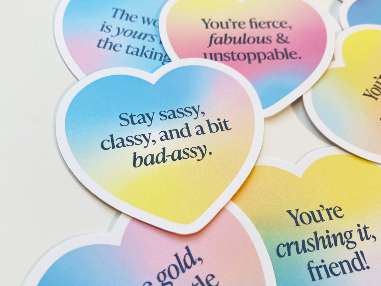 A close-up of heart-shaped gradient note cards featuring uplifting messages like Stay sassy, classy, and a bit bad-assy and You’re fierce, fabulous & unstoppable. The vibrant colors and bold text stand out against the white background.