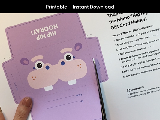 Person cutting a printable hippo gift card holder template with scissors. This DIY digital download is perfect for birthdays and kids gifts. The design features a cute hippo face and includes instructions to print, cut, and assemble at home. Ideal for handmade gift card envelopes, classroom treats, and party favors for children. A fun paper craft activity you can make instantly.
