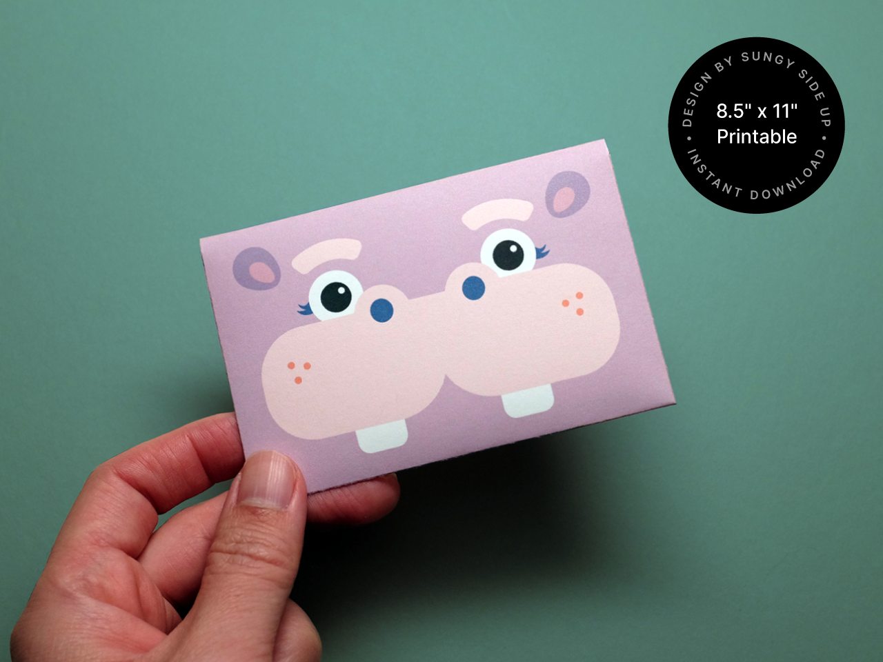 Close-up of a finished DIY hippo gift card holder being held in hand. The printable envelope features a cartoon hippo face and is perfect for birthday gifts, party favors, or classroom rewards. This digital product is an instant download you can print at home. Great for customers searching for printable gift card ideas, animal-themed stationery, or easy paper crafts for kids.