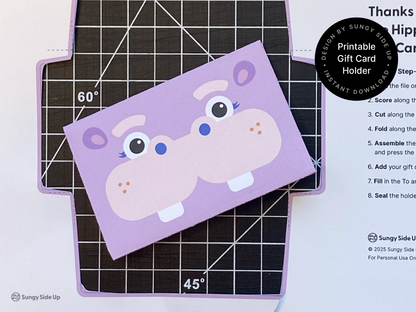 Close-up of a completed hippo gift card envelope on a cutting mat. This printable product is an instant download you can assemble at home for birthdays, kids parties, or last-minute gifts. The fun animal design makes it perfect for parents, teachers, and DIY lovers looking for creative gift wrap solutions. Easy paper craft for card gifting using cardstock and scissors.