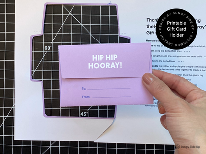 Person holding the back side of a completed printable hippo gift card holder featuring a flap with “To” and “From” lines. This digital download is a DIY paper craft for birthdays, kids gifts, and party favors. Ideal for printing at home and gifting gift cards in a fun and personal way. Great for handmade card alternatives and parents looking for creative gift wrapping ideas.