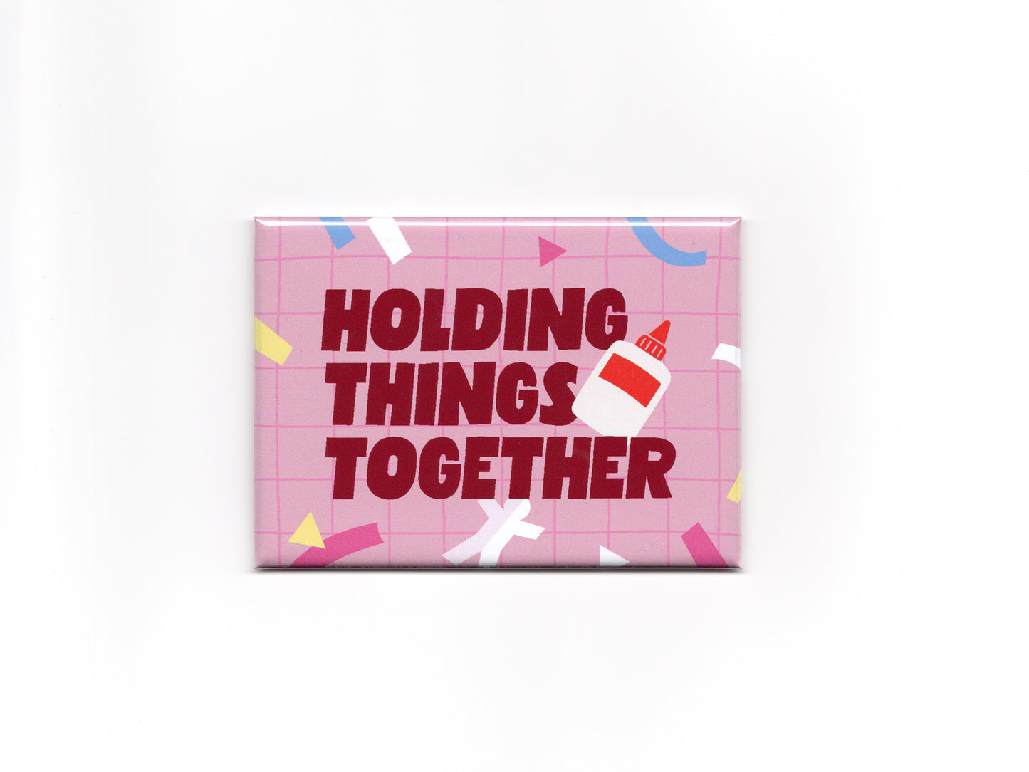 Rectangular pink magnet with a light pink grid pattern, colorful confetti accents, and bold dark red text that reads “Holding Things Together.” A small glue bottle illustration overlaps the text on the right side.