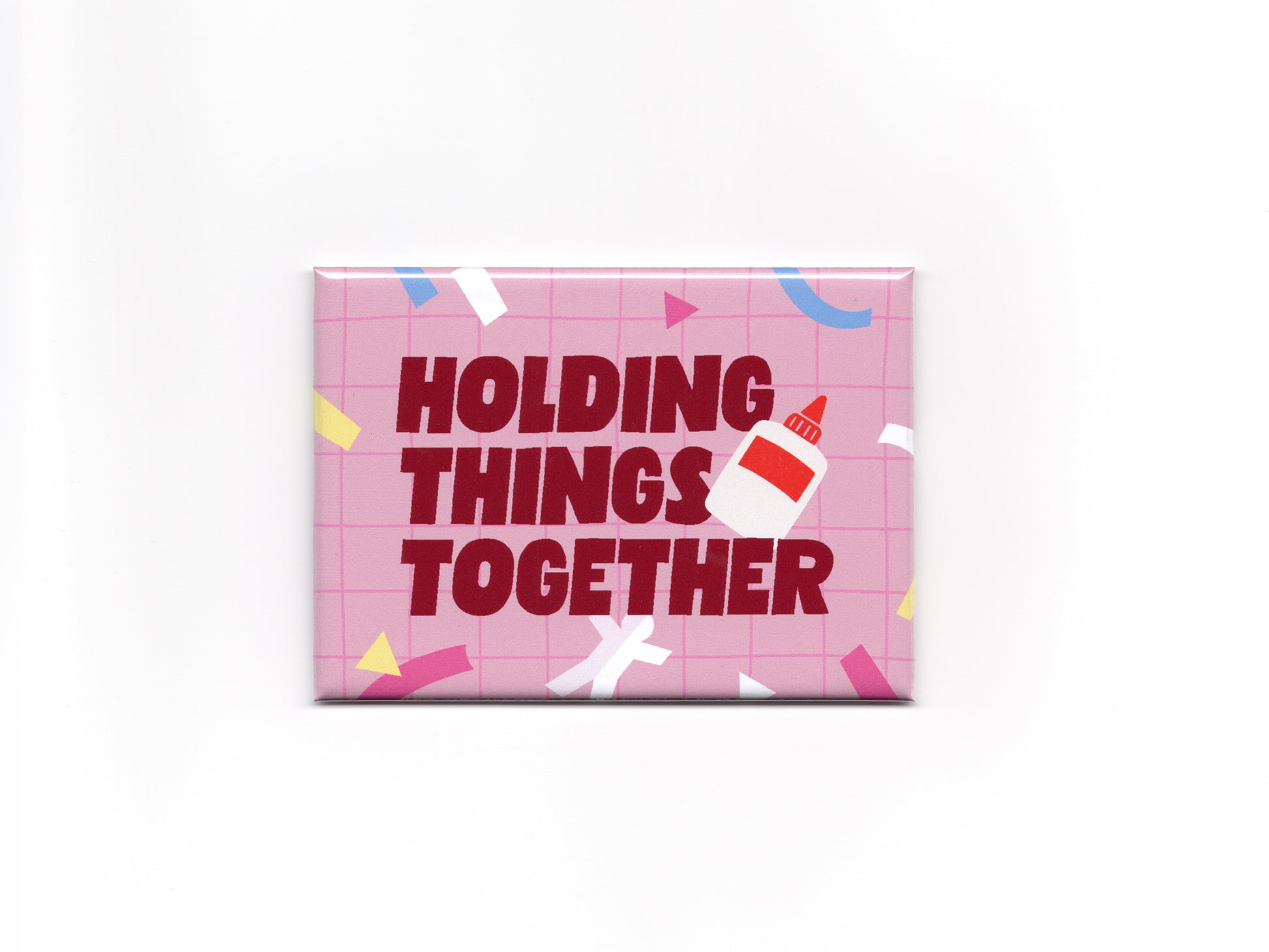 Rectangular pink magnet with a light pink grid pattern, colorful confetti accents, and bold dark red text that reads “Holding Things Together.” A small glue bottle illustration overlaps the text on the right side.