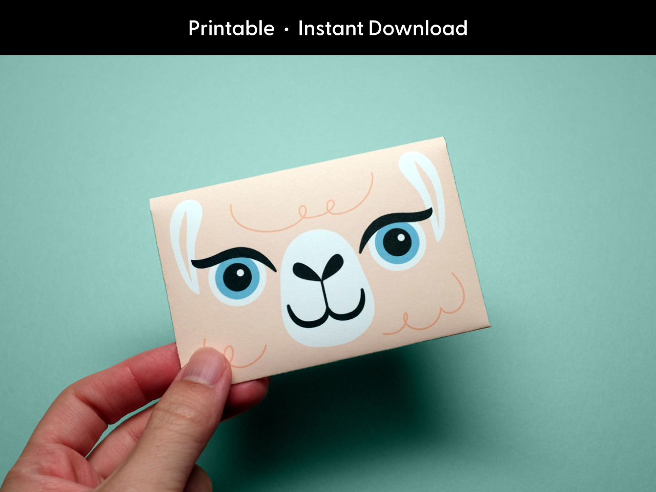 A hand holds a completed printable llama gift card holder against a teal background. The envelope features a cute cartoon llama face, ideal for kids birthday gifts, party favors, or teacher appreciation. This digital download is a fun and easy DIY craft that turns any standard gift card into a personalized and creative present. Perfect for shoppers looking for printable gift card holders with an animal theme or last-minute gifting solutions.