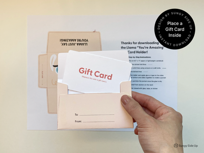 Hand inserting a mock gift card into a finished printable llama envelope. The background shows the original printed template and step-by-step assembly instructions. This image demonstrates how to use the DIY llama gift card holder, making it ideal for product listings targeting keywords like printable gift card envelope, kids birthday gift, teacher appreciation idea, and animal themed card holder for instant download.