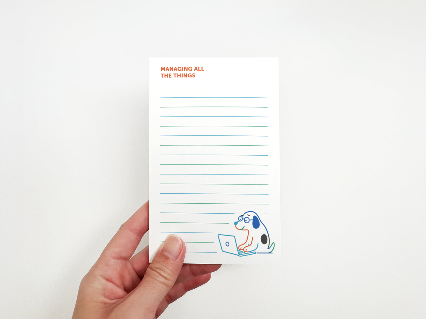 Hand holding a "Managing All the Things" notepad featuring a cute dog working on a laptop, designed for to-do lists, notes, and daily organization.