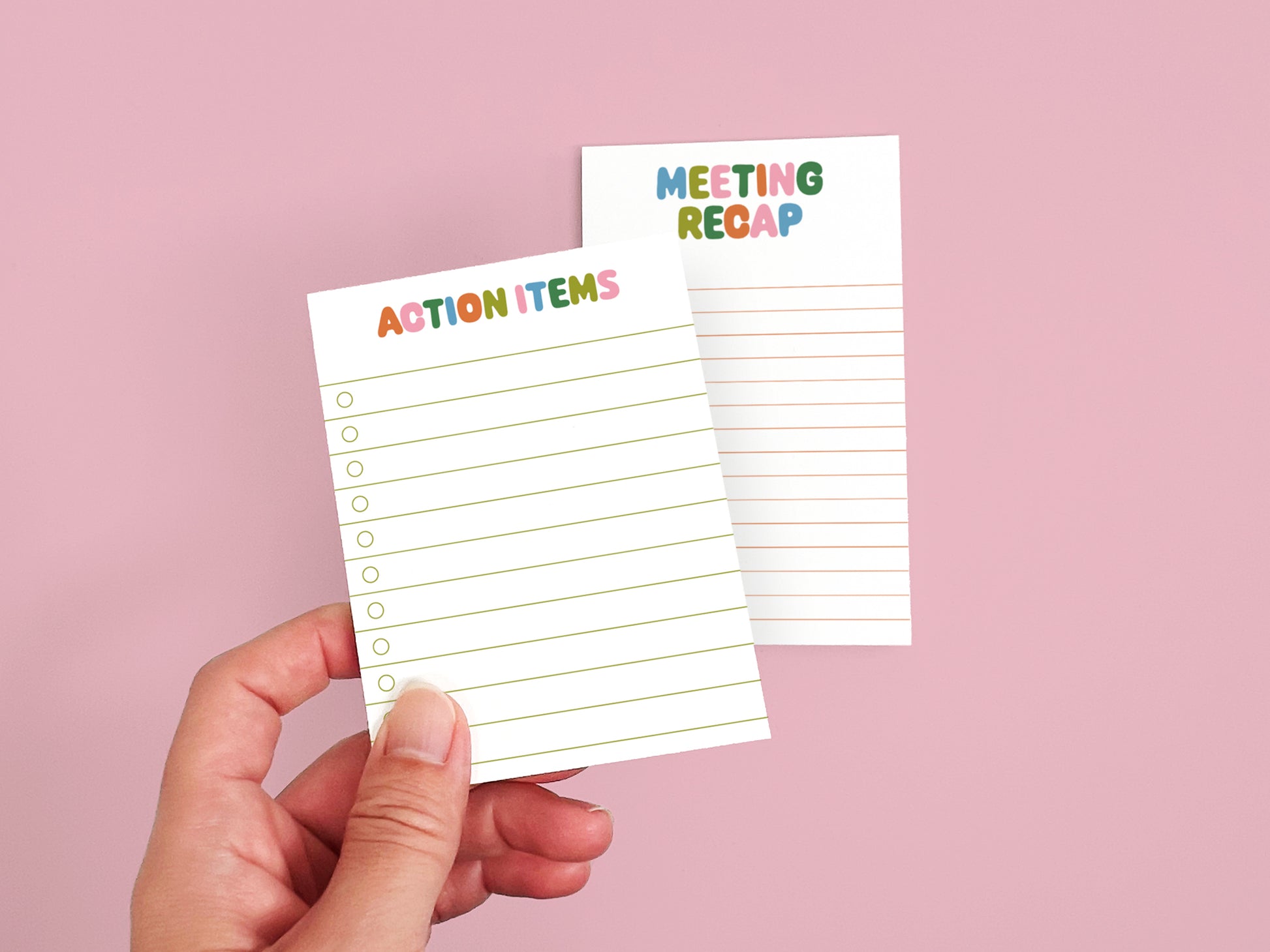 Hand holding an Action Items checklist notepad with a Meeting Recap notepad in the background on a pink backdrop.