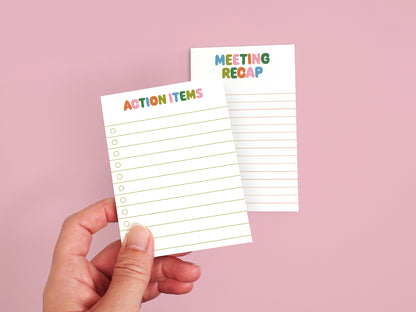 Hand holding an Action Items checklist notepad with a Meeting Recap notepad in the background on a pink backdrop.