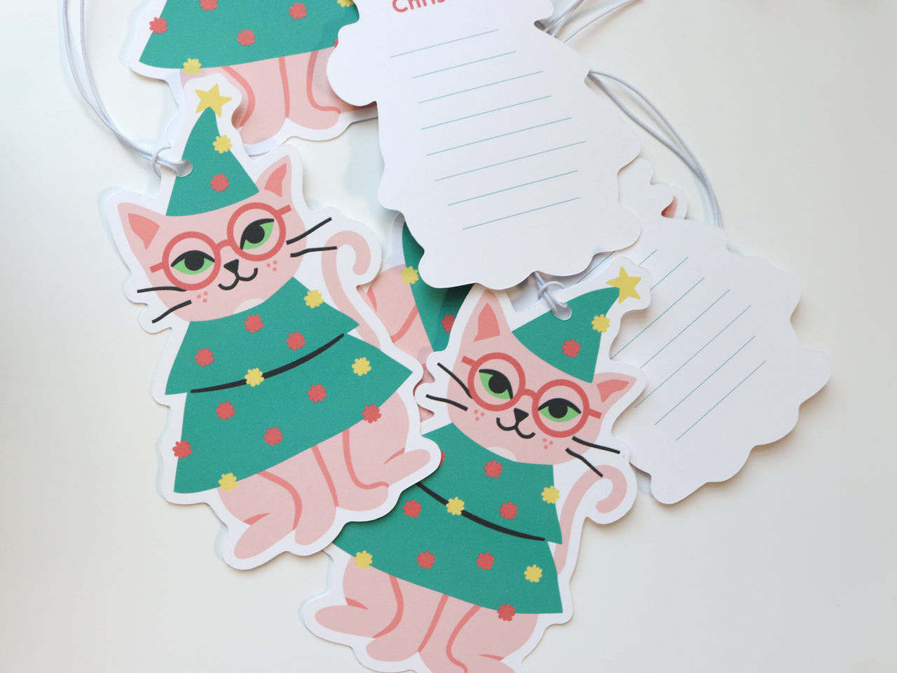 Multiple gift tags showing the front and back views. The front of the gift tags are of an illustrated cat wearing a Christmas tree outfit. The back of the gift tags has lines on the back to write your own personal message.