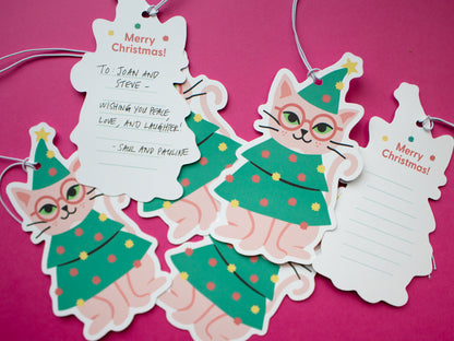 Multiple gift tags with a cat wearing glasses wearing a Christmas tree outfit spread across a magenta surface. The gift tags feature the cat illustration on the front with "Merry Christmas" on the back with lines to write a special message.
