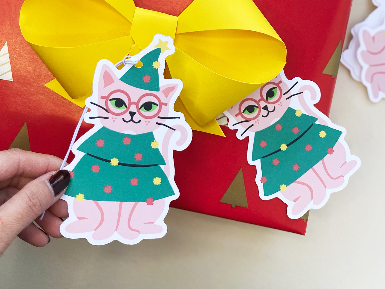 Adorable cat-themed holiday gift tags featuring a pink cat with glasses dressed as a Christmas tree, accented with bright decorations. A creative touch for wrapping Christmas presents, ideal for cat lovers and festive celebrations.