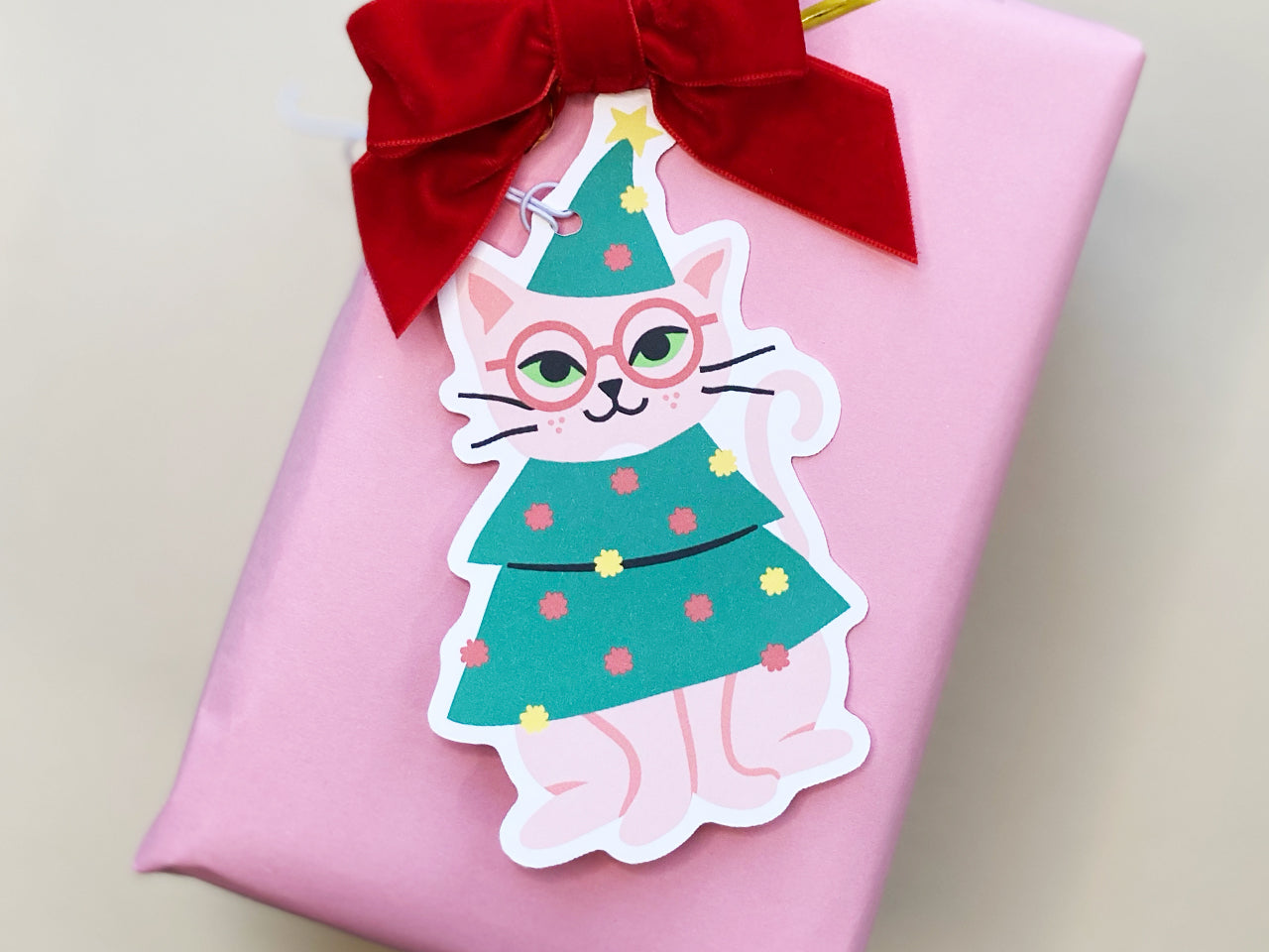 Holiday gift wrapping made fun with unique cat-themed gift tags, featuring a pink cat in a Christmas tree costume. Paired with 'Merry Christmas!' tags for adding a personal and festive touch to Christmas presents.