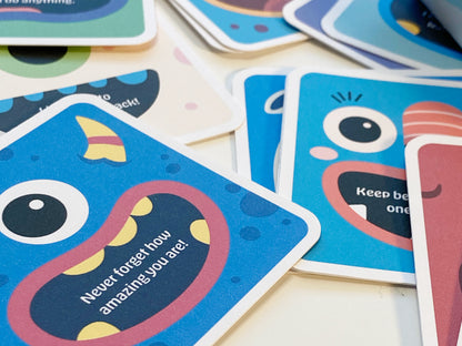 A close-up of colorful monster-themed lunch box notes for kids featuring playful cartoon monster faces and positive, encouraging messages. The cards are square-shaped with rounded corners and are laying on a white surface, showcasing vibrant designs.