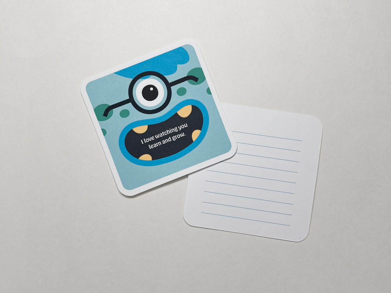 A single blue monster-themed note card with a cheerful one-eyed cartoon character and the message, I love watching you learn and grow. The encouraging note card is displayed alongside its blank lined back on a white background.