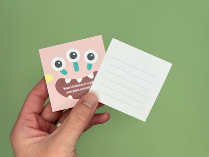 Hand holding two square monster lunch box note cards on a green background, showing a colorful monster design on the front and a lined blank back for handwritten messages, handmade kids lunchbox notes for school lunches and backpacks.
