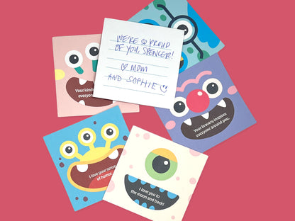 Flat lay of colorful square monster lunch box note cards on a pink background, including one lined card with a handwritten message, showing handmade kids lunchbox notes with playful monster designs for school lunches and backpacks.