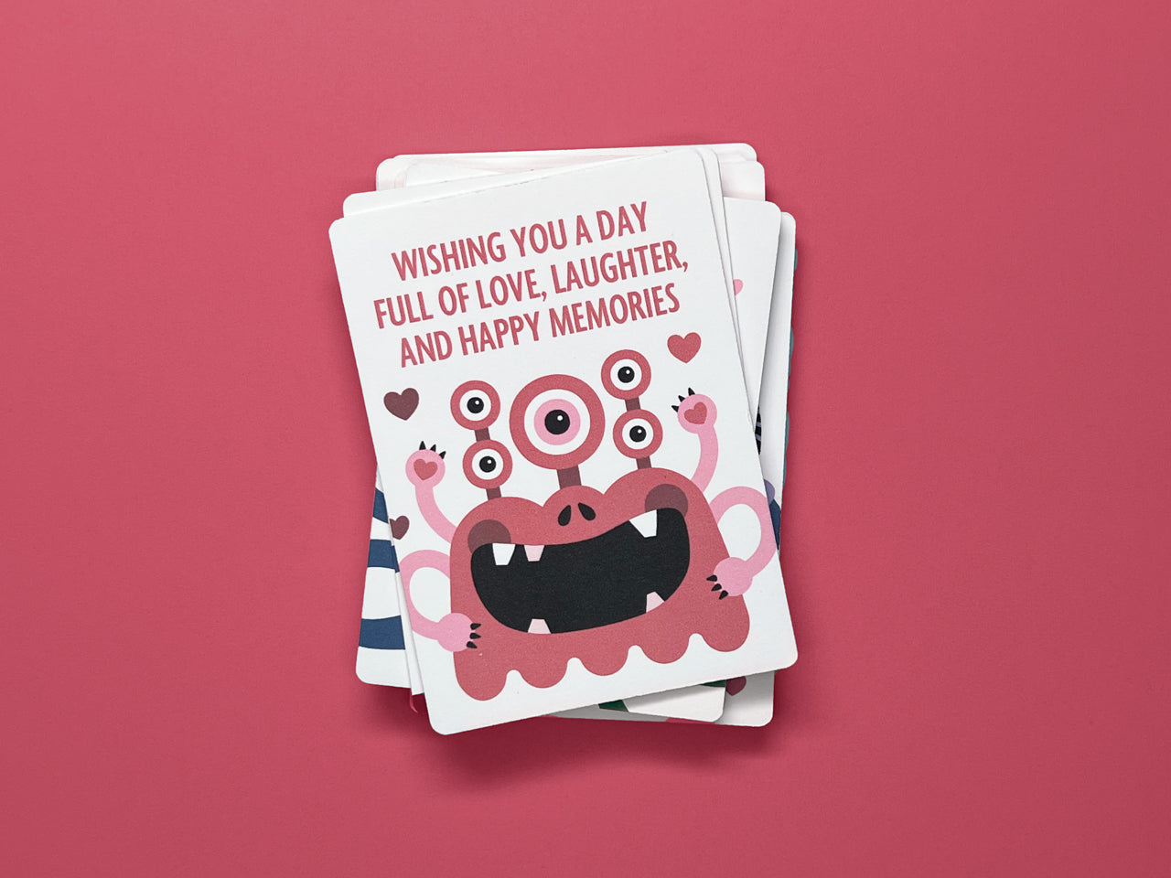 A stack of monster-themed Valentine's Day cards against a deep red background. The top card features a cheerful pink monster with three eyes and a playful smile, and surrounded by heart accents. This fun design is part of a set of 24 Valentine Cards.