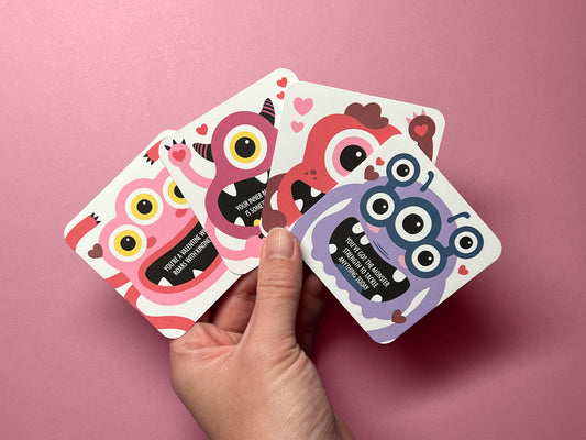 A hand holding four colorful monster-themed Valentine lunch box notes against a pink background. Each card features a unique monster illustration paired with an encouraging message. These lunch notes are perfect for kids, Valentine’s Day, and parties