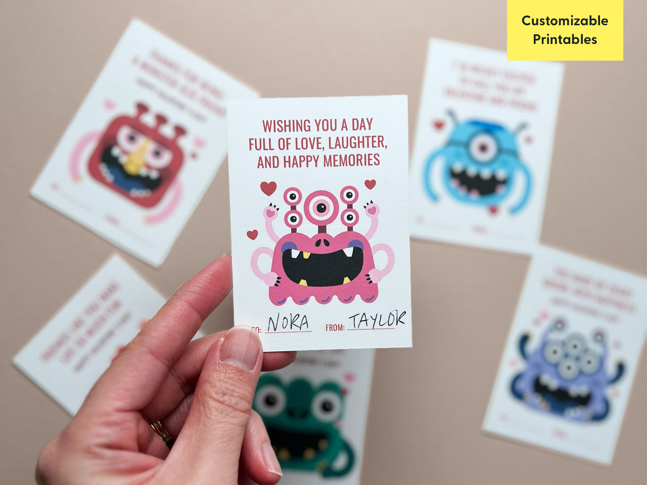 A close-up of a pink monster-themed Valentine card with the text, Wishing you a day full of love, laughter, and happy memories. The card features a smiling pink monster with multiple eyes and hearts around it.