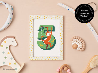 A framed printable monthly milestone card for 5 months, featuring a monkey design and bananas. Displayed on a pastel pink background with playful nursery decor, including a wooden rocking horse and baby toys, highlighting its dual use as wall art.