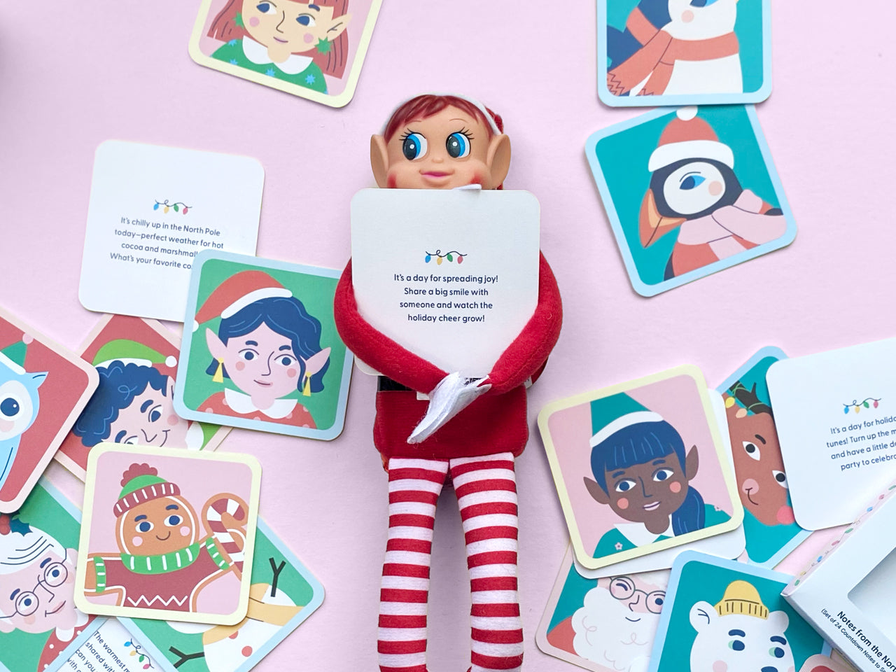 Christmas elf doll wearing a red costume holding a note card from the Notes from the North Pole set, surrounded by colorful North Pole character illustrations ideal for holiday excitement.