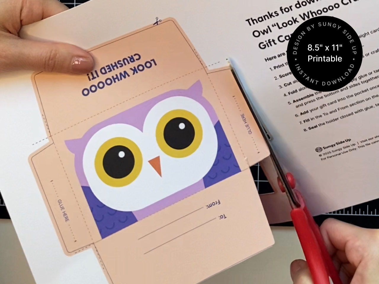 Hands cutting out a printable owl gift card holder template with red-handled scissors on 8.5 x 11 inch paper. DIY craft file includes glue tabs and printed fold lines for easy assembly. Perfect image for showcasing the ease of making a handmade graduation or thank you card using a digital download. Great for Shopify product listings targeting classroom or celebration gifts.
