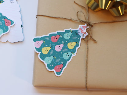 A kraft-wrapped Christmas gift tied with twine and adorned with a whimsical Partridge in a Pear Tree gift tag. The tag features a tree with colorful smiling pears and a bird in a red hat, perfect for festive holiday wrapping.