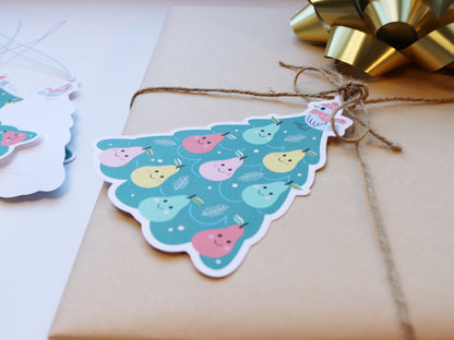 A close-up view of a kraft-wrapped gift tied with twine, showcasing a colorful Partridge in a Pear Tree tag with smiling pears and a bird illustration.