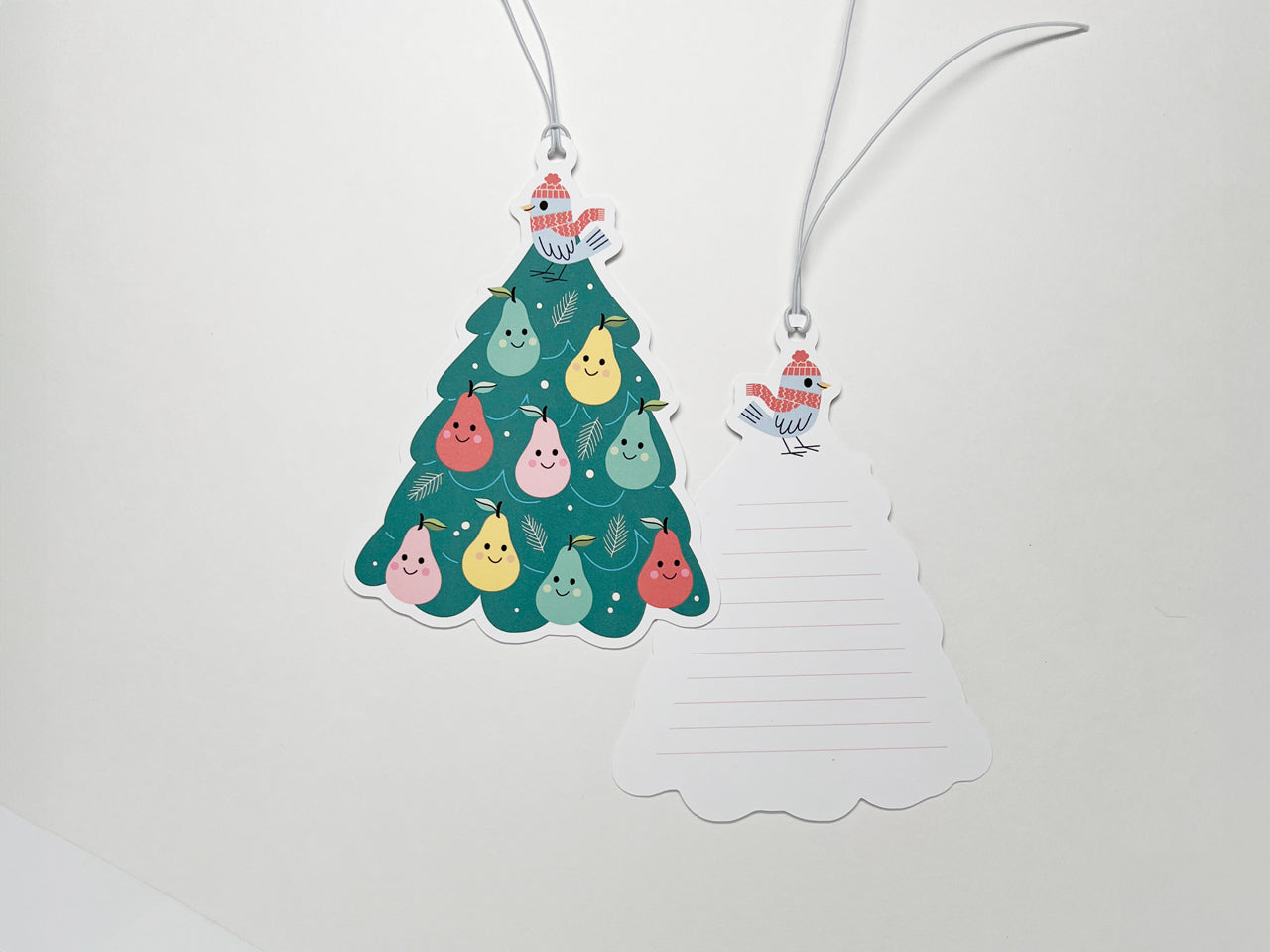 A double-sided gift tag shaped like a Christmas tree, featuring a Partridge in a Pear Tree design with smiling pears and a gray bird. The back of the tag includes lined space for personalized messages, tied with a white string for easy attachment.