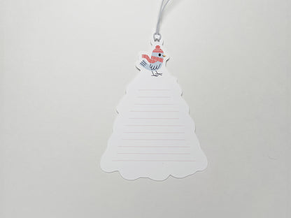 A close-up of the back of a Christmas gift tag shaped like a tree, with lined space for handwritten notes and a small bird illustration wearing a red winter hat and scarf at the top. Pre-attached white elastic string for easy attachment to gifts.